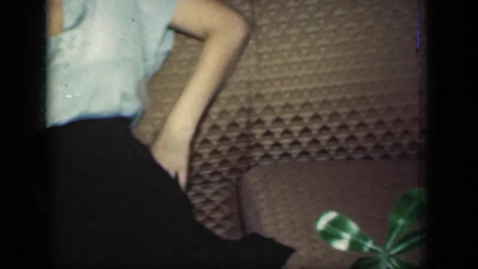 A partially cropped frame shows the woman's blouse, arm, dark skirt, and the brown quilted sofa in the same domestic interior.