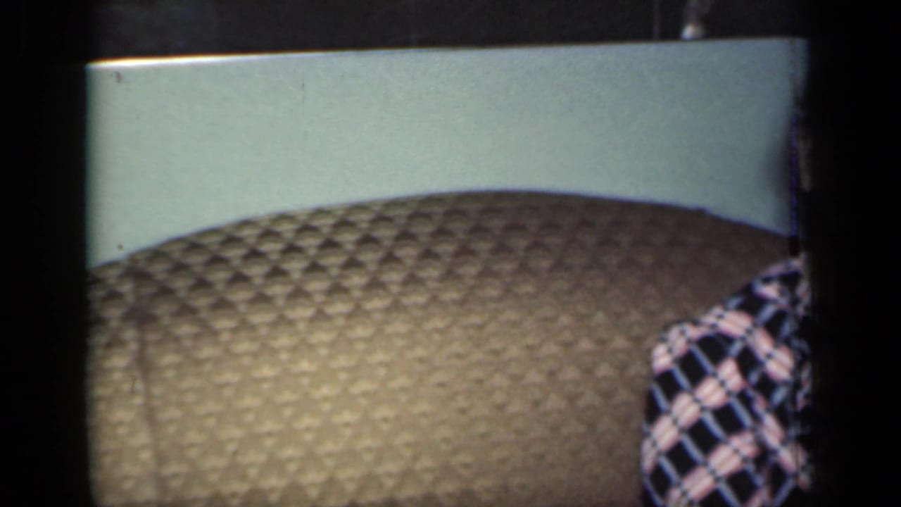 Older woman partly cropped on a brown quilted couch in a domestic room.