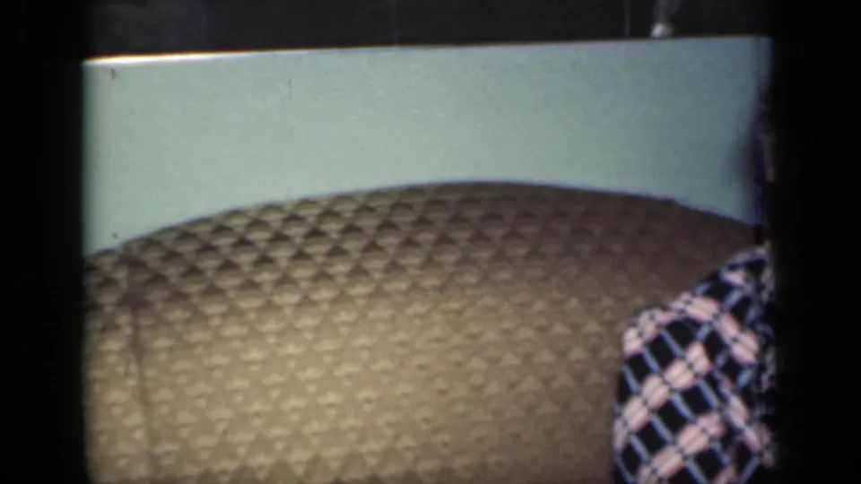 In a 1949 New York home-movie frame, an older woman is partly cropped while seated on a brown quilted couch.