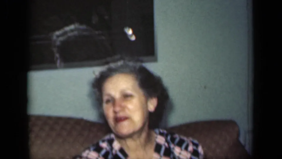 The older woman appears to speak or react while seated on the couch in the 1949 New York domestic interior.