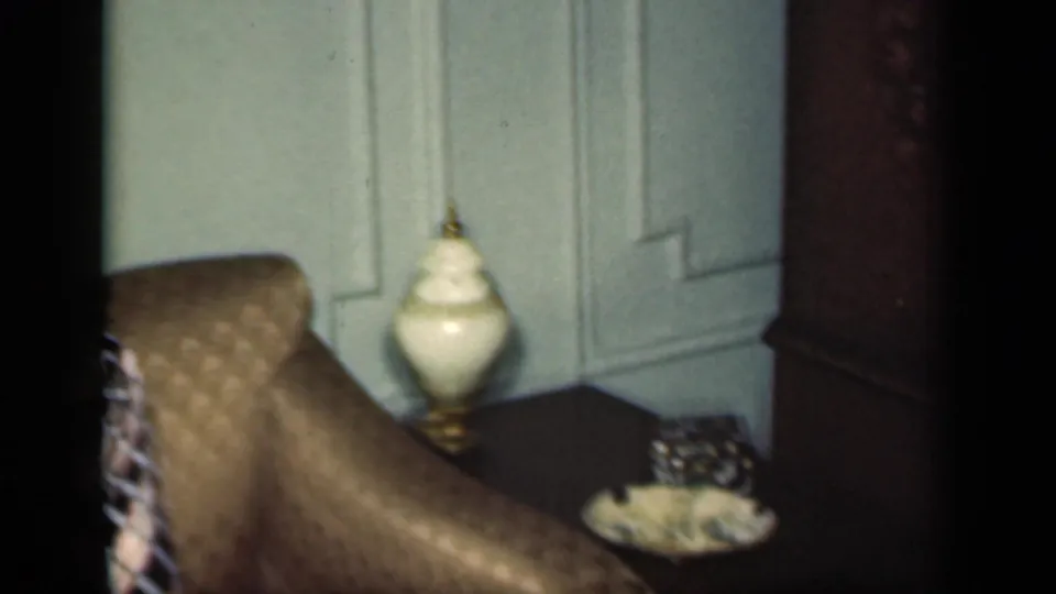 A 1949 New York home interior detail shows a side table, white lamp, decorative bowl, couch edge, and paneled door.