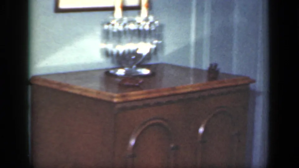 A polished wooden cabinet holds a glass candle holder with candles, set against pale paneled walls in the home interior.