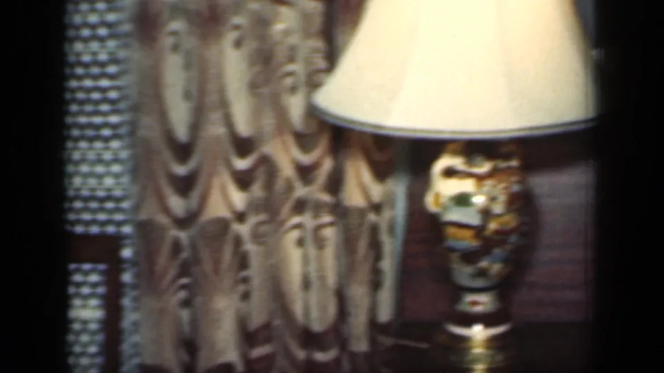 1949 New York interior detail with a shaded decorative lamp on a wood table, patterned curtains behind it, and visible film-frame borders.