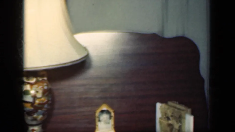 1949 New York home interior showing a lamp on a wooden table with a small framed picture and pale curtain in the background.