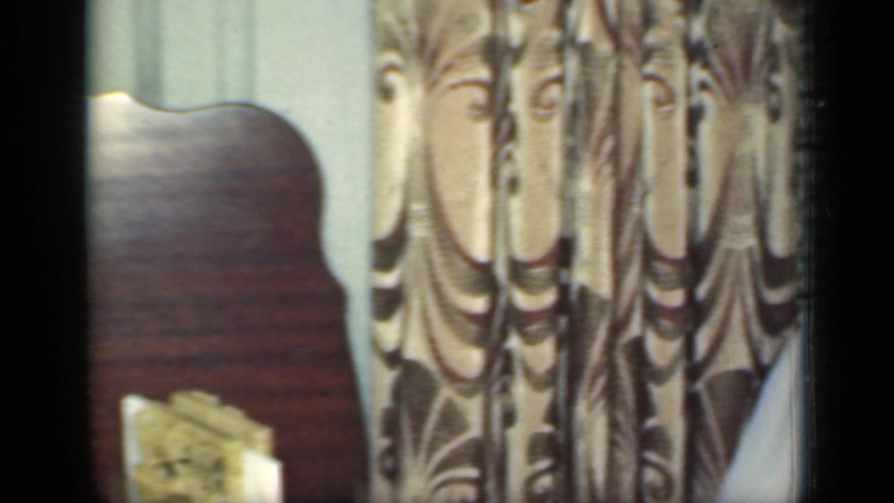 1949 New York interior detail with patterned curtains, a wooden surface and a small upright book or framed object near the window area.