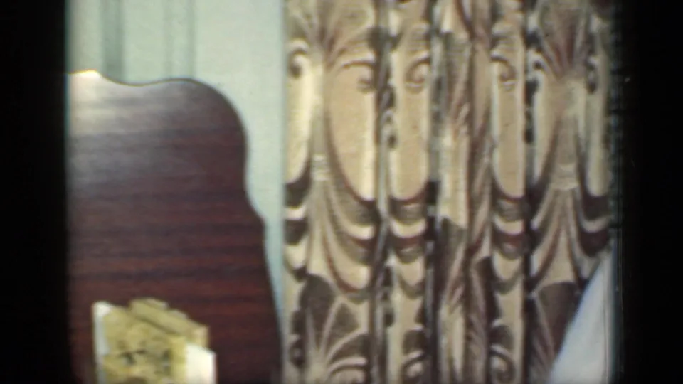 1949 New York interior detail with patterned curtains, a wooden surface and a small upright book or framed object near the window area.