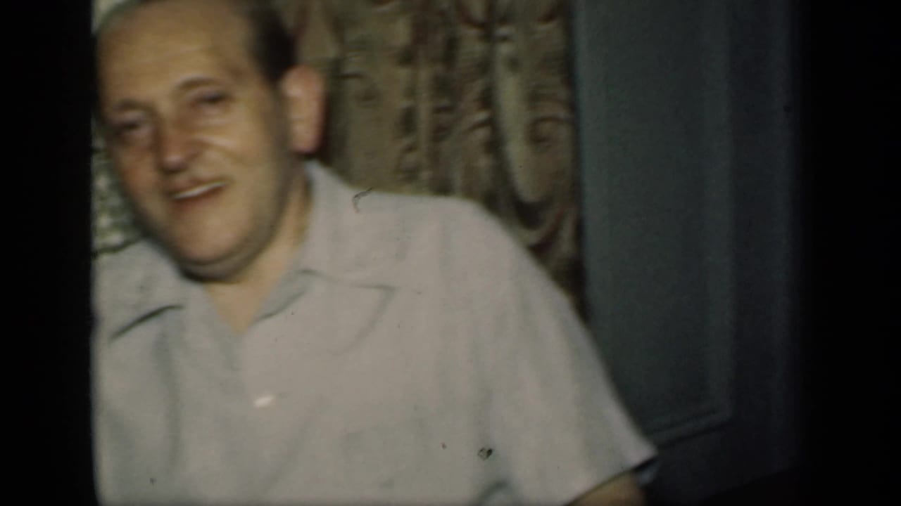 Adult man in a light collared shirt smiles beside patterned interior decor.