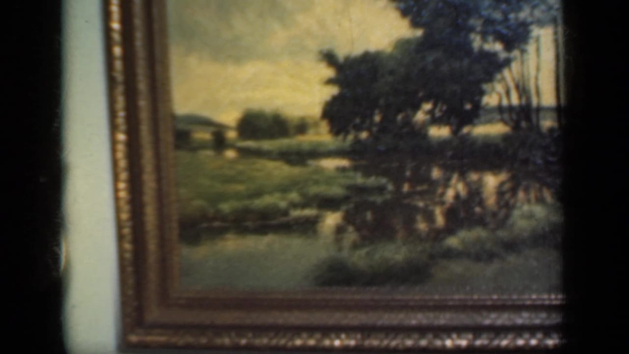 Framed landscape painting with trees and water on a pale interior wall.