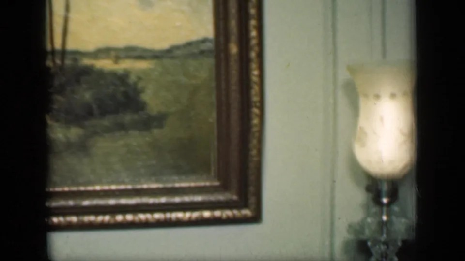 1949 New York home-movie frame showing part of a framed landscape painting and a small lamp with a frosted shade below it.