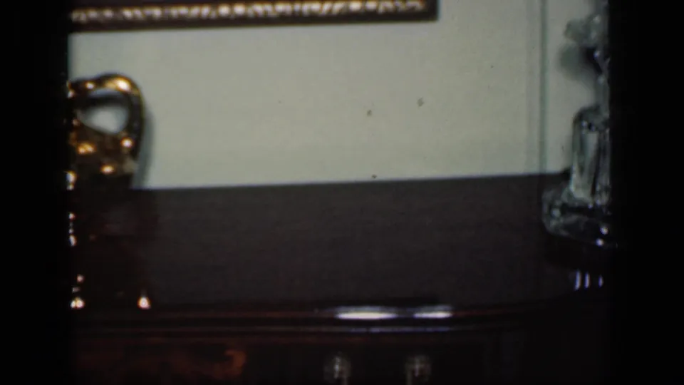 1949 New York interior frame showing a glowing lamp, a dark wooden console, and a glass object beneath a framed landscape painting.