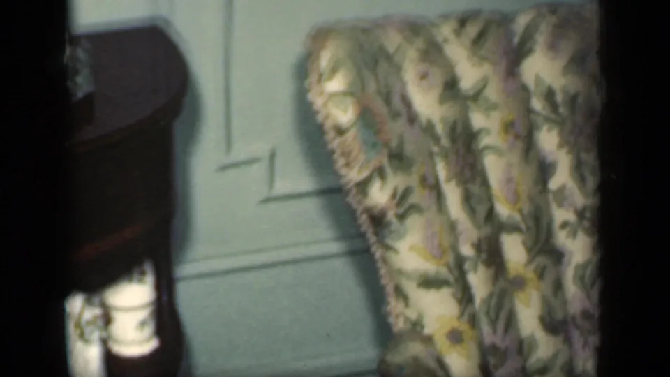 1949 New York 8mm frame showing a green-and-white floral chair next to a dark wooden table in a private room.