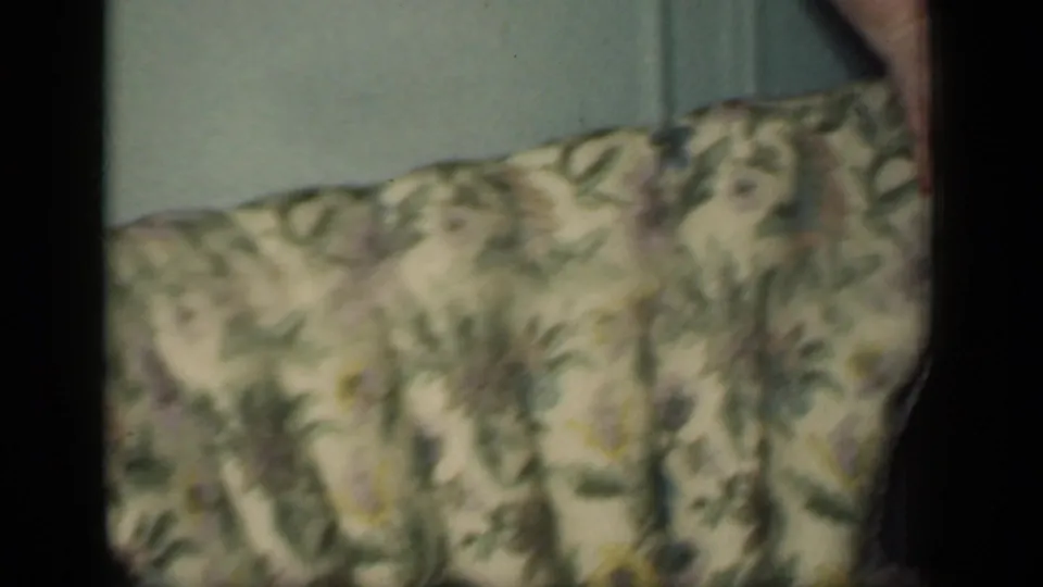 1949 New York home-movie frame with a close view of floral chair upholstery and a hand entering near the top edge.