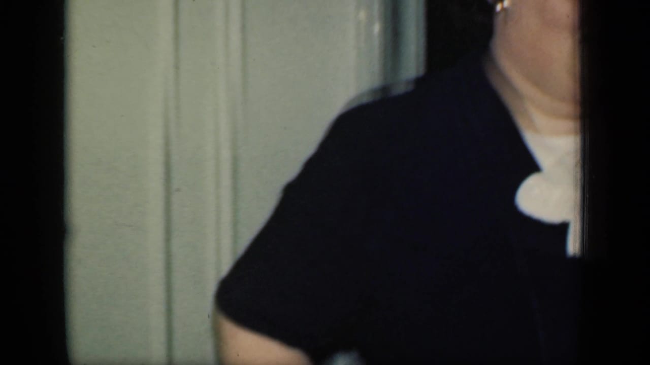 Partial close view of a woman in a dark jacket and white collar near a doorway.