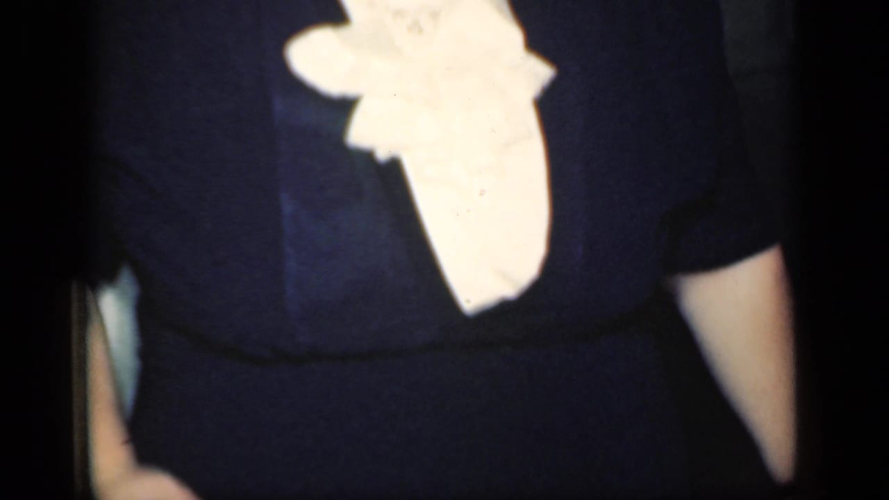 Close cropped 1949 home-movie frame showing dark clothing and a bright white ruffled blouse detail indoors.