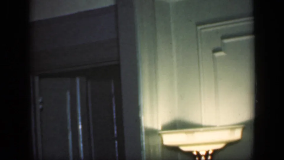 A dim 1949 New York home interior shows green wall paneling, molding, and a softly glowing floor lamp.