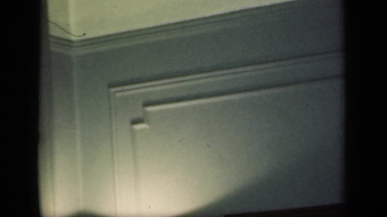 Dim paneled wall with dark film edges and soft light near the lower left.
