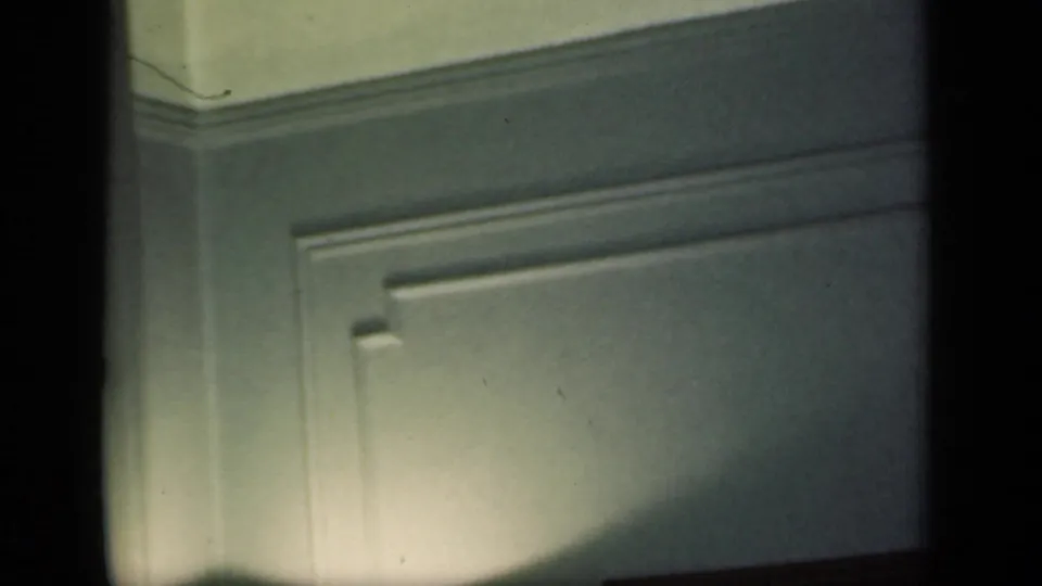 1949 New York 8mm frame showing a dim private interior wall with molding, shadow and visible film-frame edges.