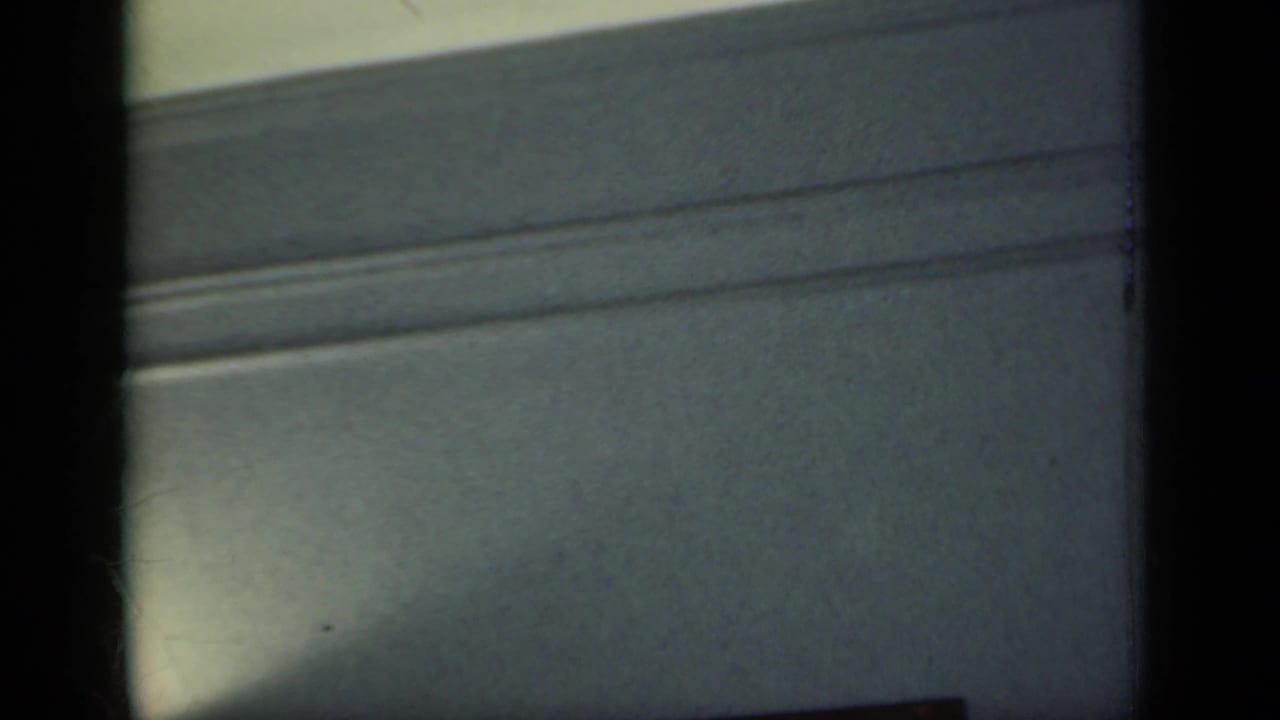 1949 New York home-movie frame of upper wall molding and muted interior paint, partly obscured by dark film borders.