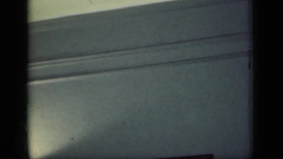 1949 New York home-movie frame of upper wall molding and muted interior paint, partly obscured by dark film borders.