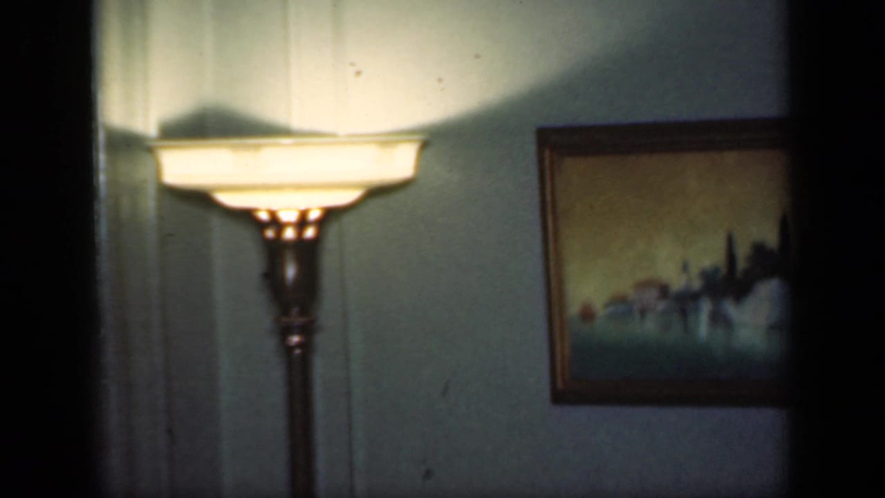 Floor lamp glowing beside framed wall art in a dim living room.