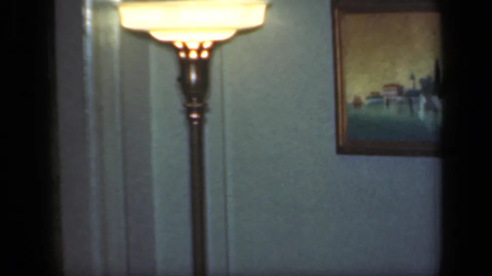 The camera holds on a lit floor lamp and framed wall picture in a 1949 New York private living-room interior.