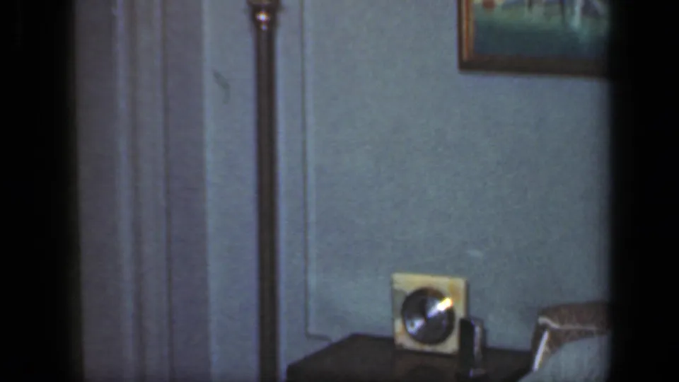 1949 New York home-movie frame showing a tabletop radio, small clock, framed art, and part of a sofa in a private living room.