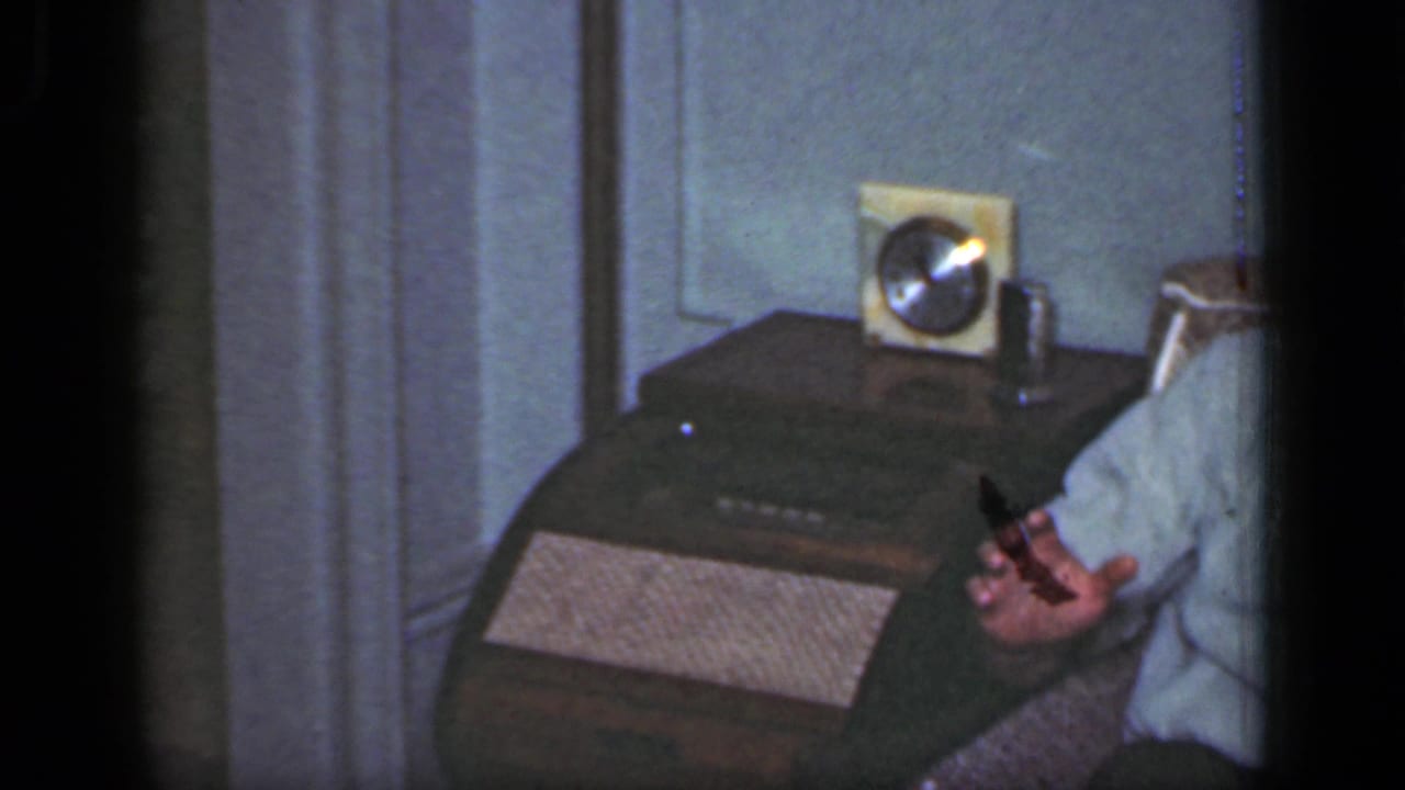 Partial view of a seated man gesturing beside a wooden table with a small radio.