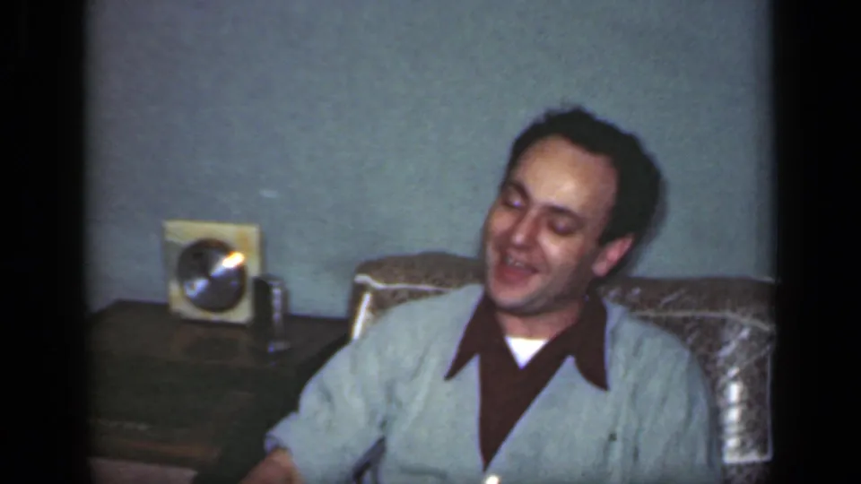 1949 New York home-movie still of a man leaning back in an armchair near a side table and radio.