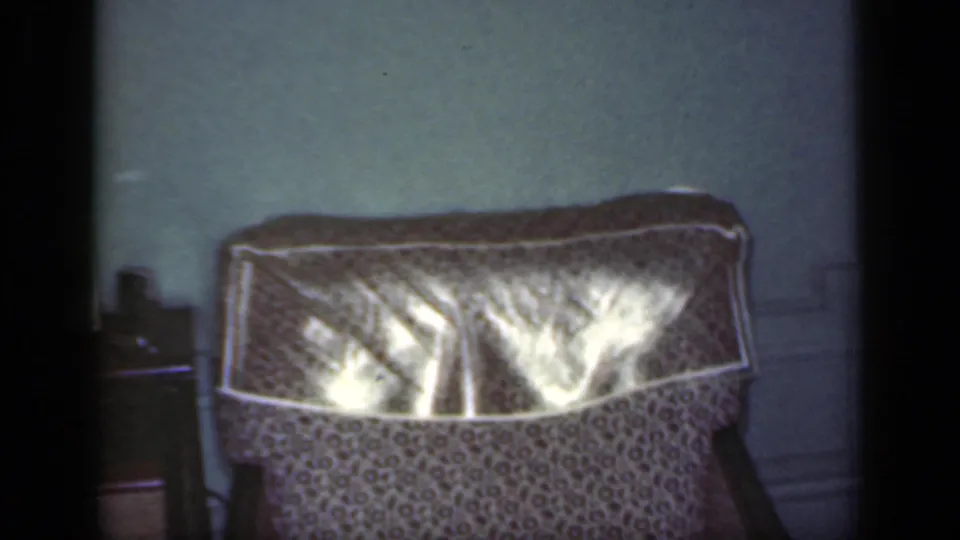 The shot settles on the patterned armchair and shiny protective cover in the 1949 New York home interior, with the person mostly out of frame.