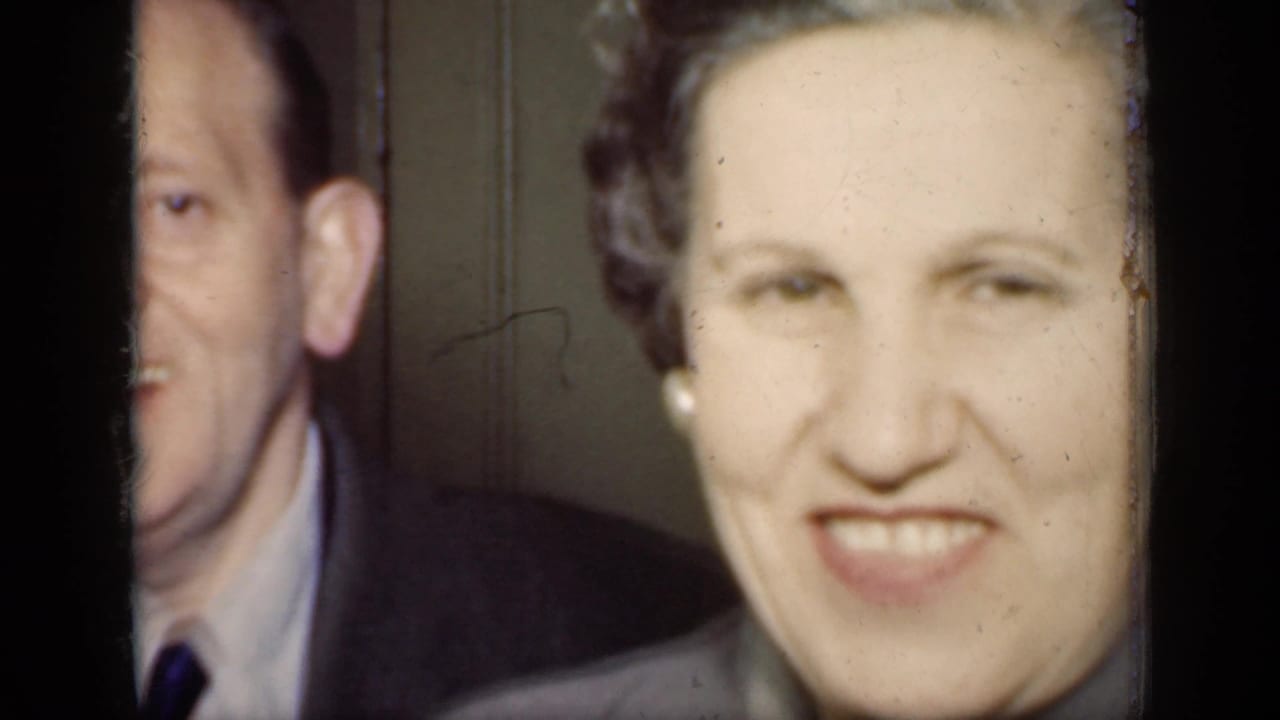 Smiling man in suit partly visible beside a smiling woman indoors.