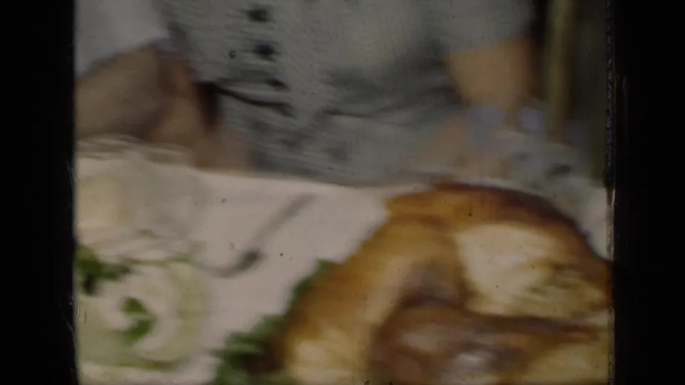 1949 New York home-movie frame showing a woman in a striped dress near a roasted turkey on a set dining table.