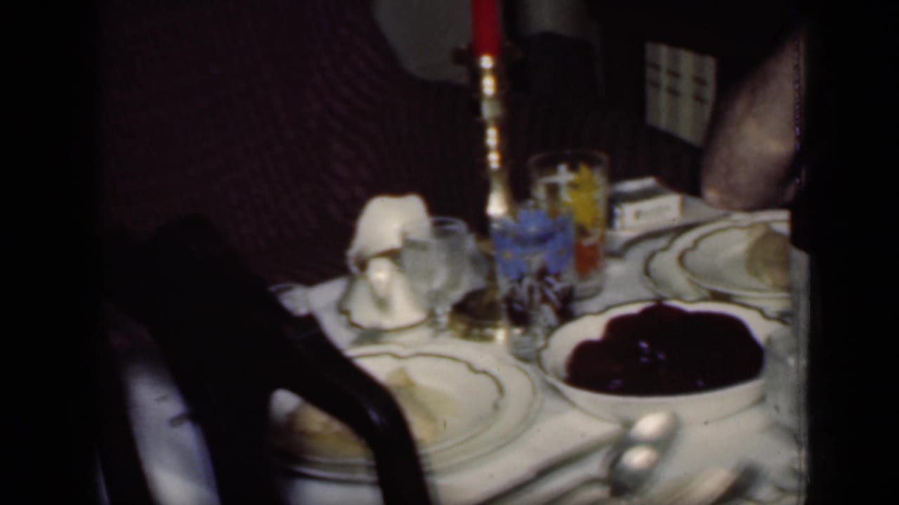 Set dining table with red candle, plates, glasses, and bowl of dark sauce.