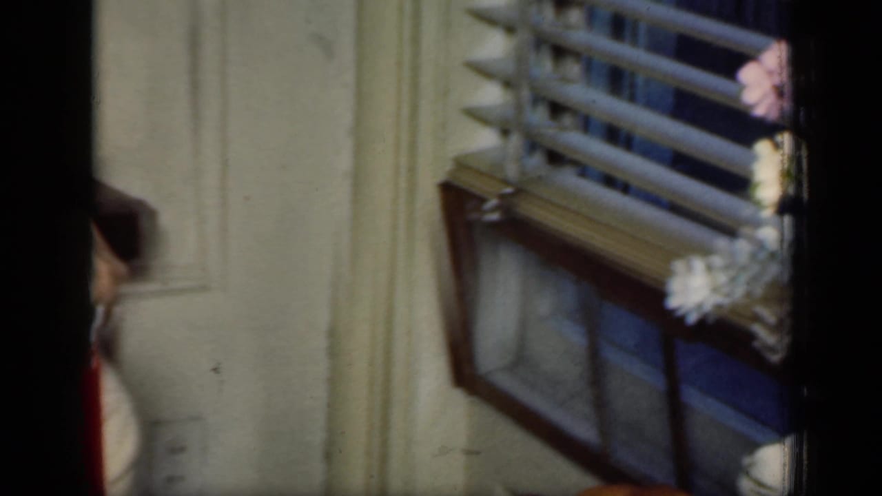 Window blinds and a partial hand appear beside the edge of an interior room.