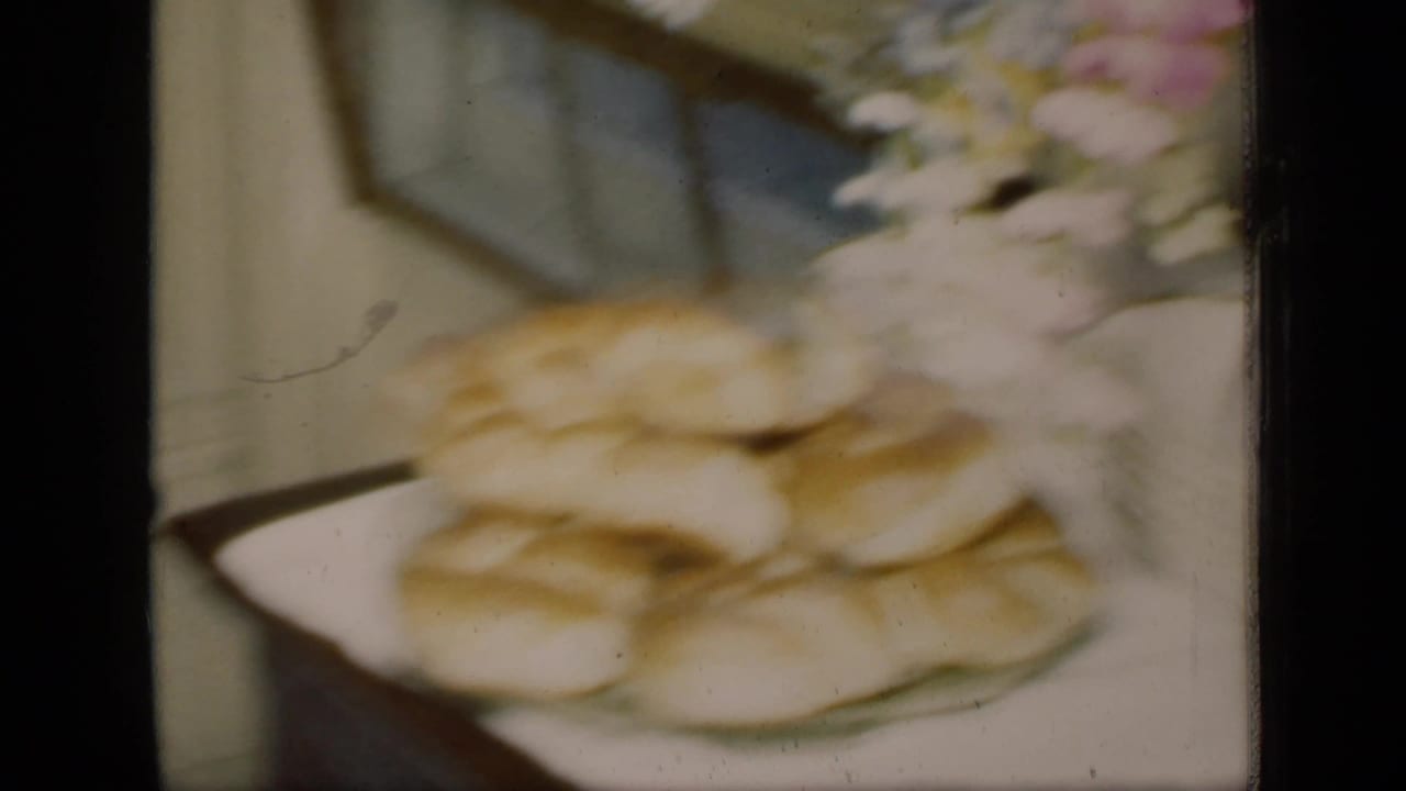Soft-focus plate of bread or rolls beside flowers on an indoor surface.
