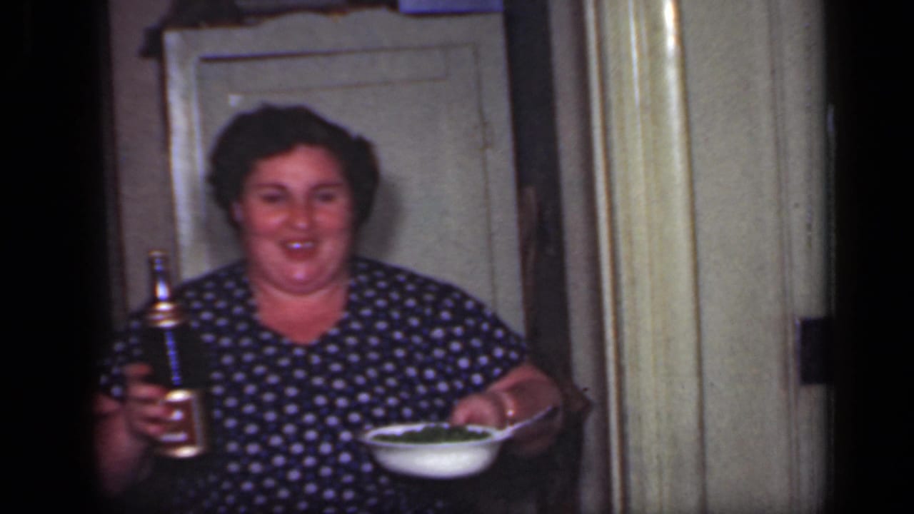 Woman in a blue polka dot dress holding a bottle and a bowl in a doorway.