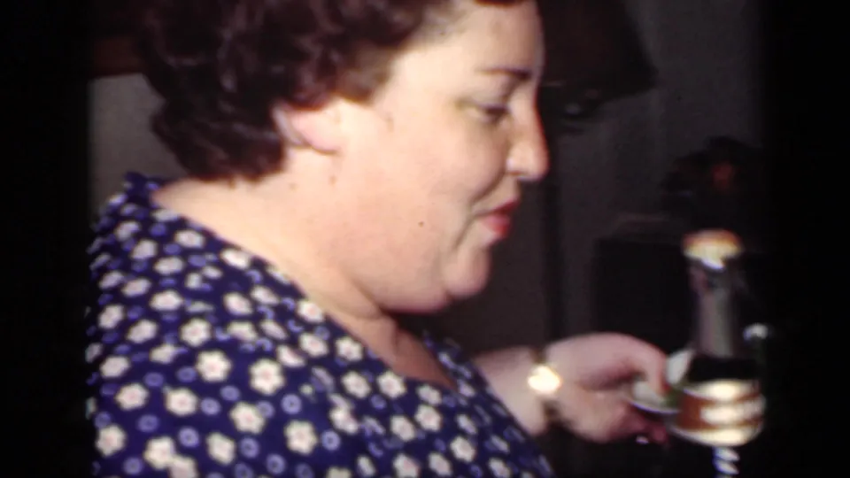 Side view from 1949 New York home-movie footage showing an adult woman in a polka dot dress holding a bottle and dish indoors.