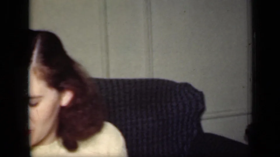 A woman in profile looks downward near a dark couch and light wall in this 1949 New York home-movie frame.