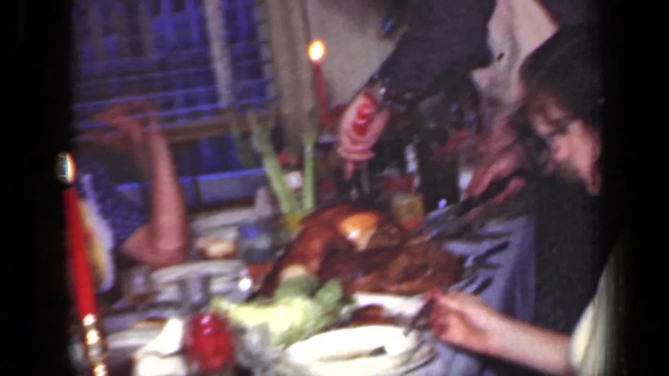 Man carves or serves a roasted turkey at a 1949 New York holiday dinner table as a woman sits nearby in the softly lit room.