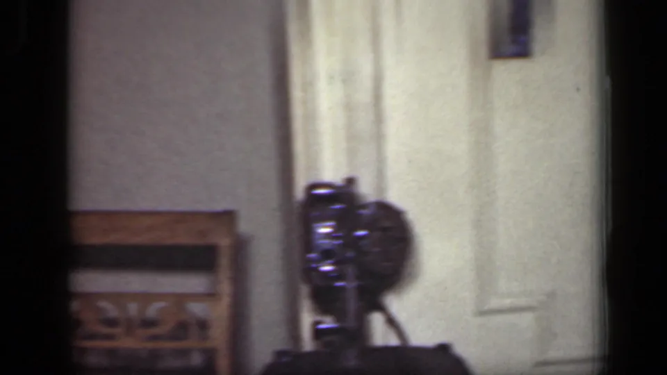 A dim 1949 New York interior shows a closed door, chair, and small camera or projector-like object on a table.