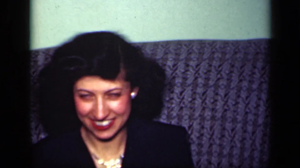 A second adult woman in dark clothing laughs near the same textured sofa in the 1949 New York home setting.