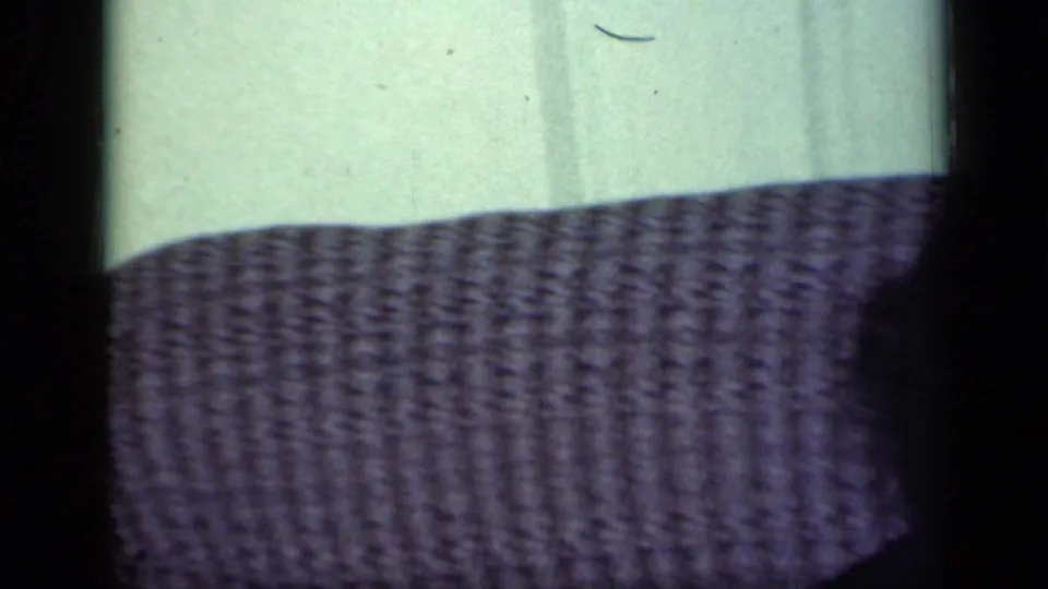 The camera catches the textured grey sofa and pale wall, with only a partial dark figure visible at the right edge.