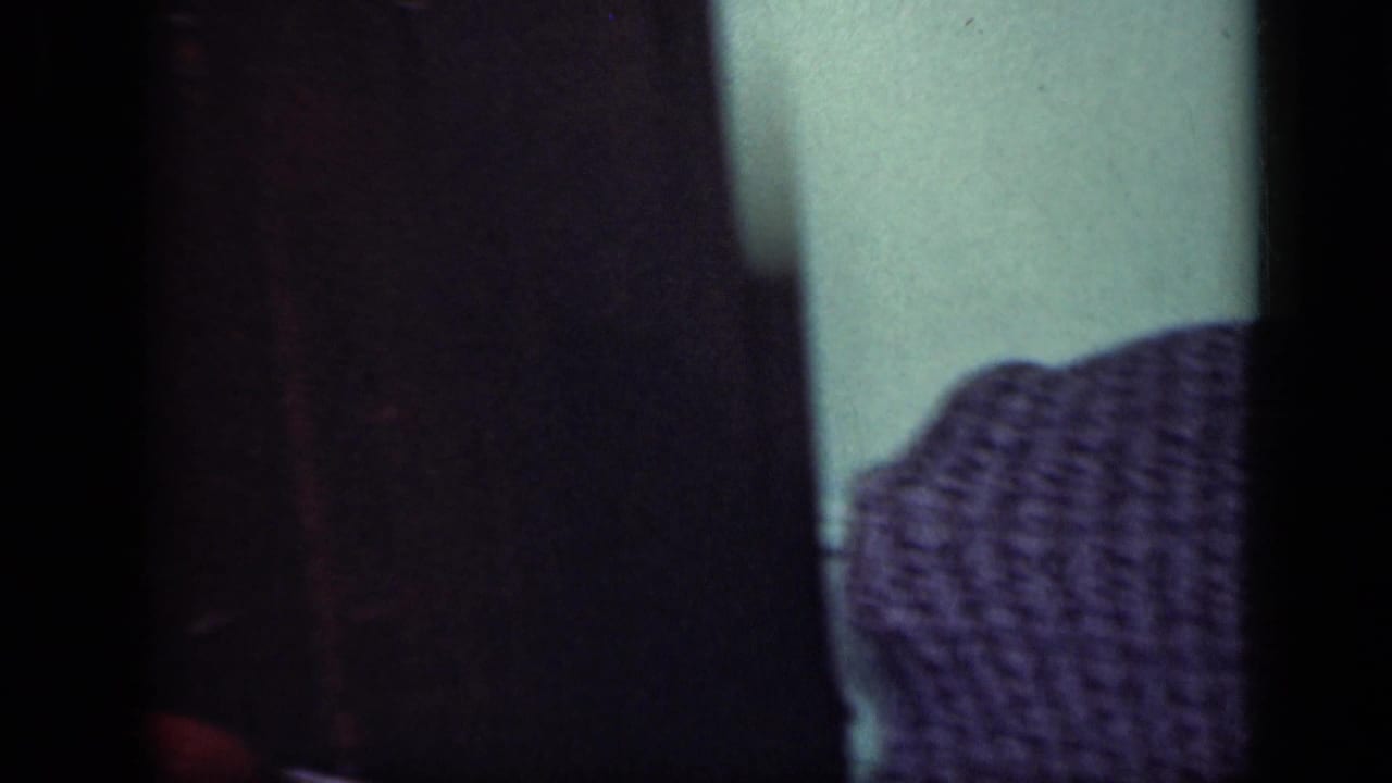 1949 New York home-movie frame showing a close, dark view of textured purple fabric near a pale green indoor wall.