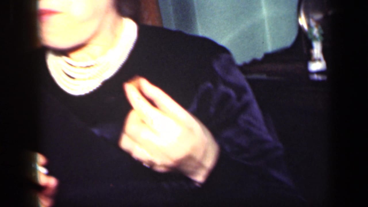 Partly cropped adult in dark clothing holding a cigarette in a dim room.