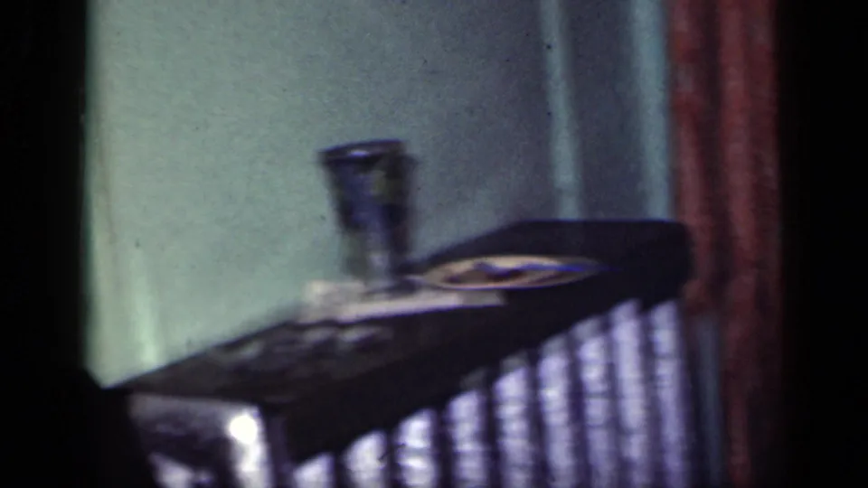 A 1949 New York home-movie frame shows a record player or turntable in a private room near curtains and a green wall.