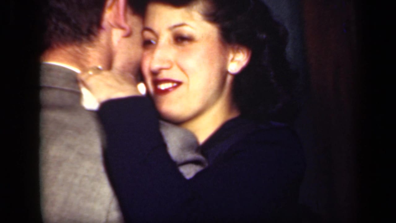 Woman in a dark blue coat smiles while leaning close to a man indoors.