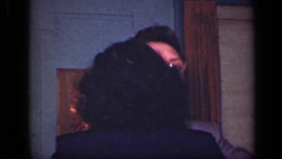 In a 1949 New York home-movie frame, the couple is partly obscured while embracing near a paneled door and framed wall art.