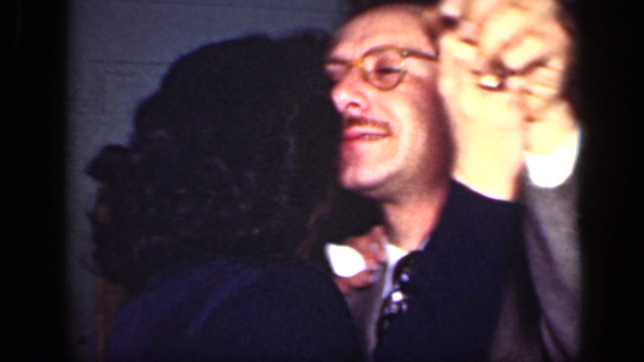 Close view of a man in glasses dancing with a woman inside a dim room.