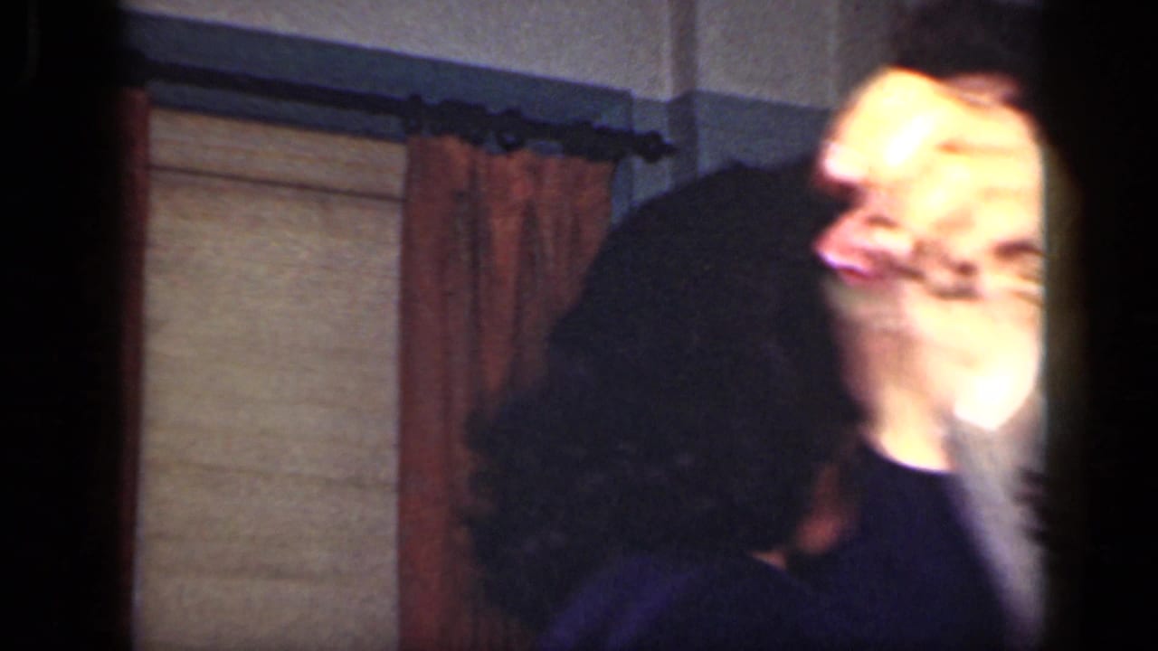 1949 New York domestic frame with a woman in pearl-like earrings dancing near a man, framed by curtains and dark film edges.