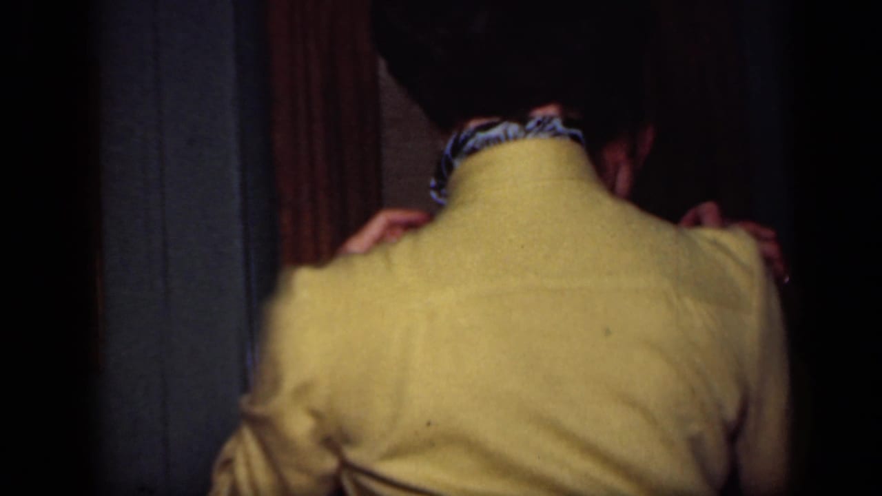1949 New York home-movie frame showing a woman in a yellow sweater and scarf dancing in a dark private interior.