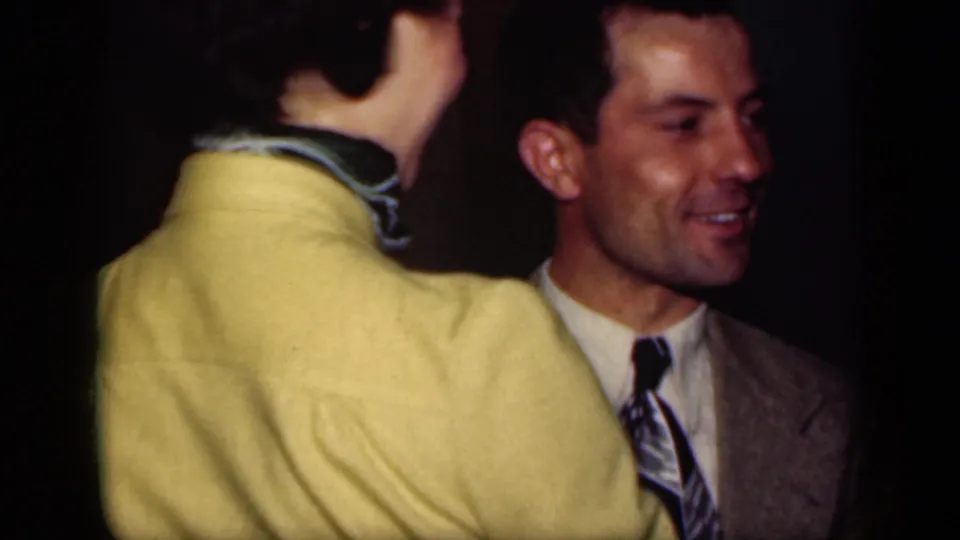 1949 New York 8mm frame of a woman in a yellow sweater dancing with a smiling man in a gray suit and patterned tie.